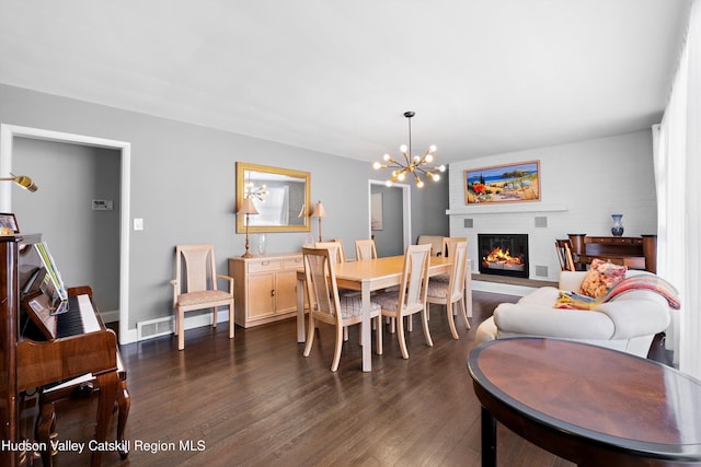 dining area featuring dark wood finished floors, visible vents, a glass covered fireplace, a chandelier, and baseboards
