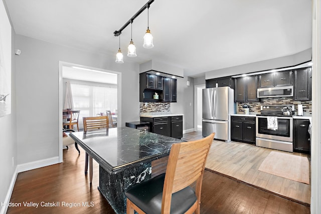 kitchen featuring stainless steel appliances, dark wood-style flooring, decorative light fixtures, and dark cabinets