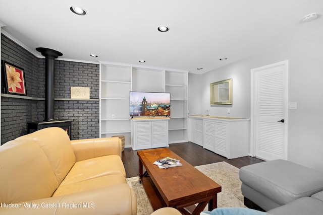 living area with recessed lighting, a wood stove, dark wood finished floors, and brick wall