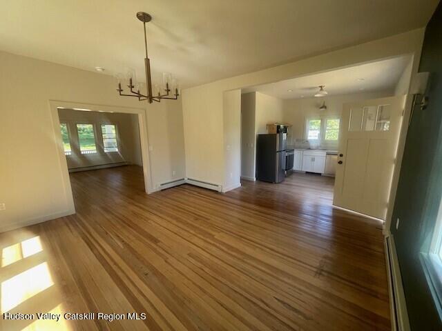 unfurnished dining area featuring a baseboard heating unit, an inviting chandelier, and dark wood-type flooring