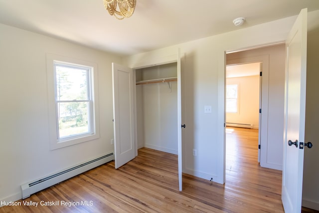 unfurnished bedroom featuring light wood-type flooring, a closet, and baseboard heating