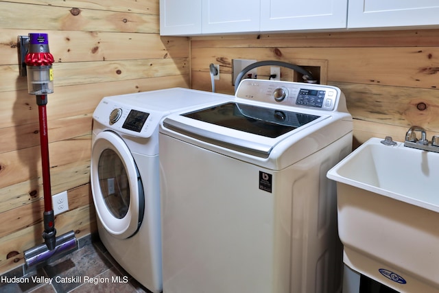 washroom with cabinets, independent washer and dryer, wooden walls, and sink