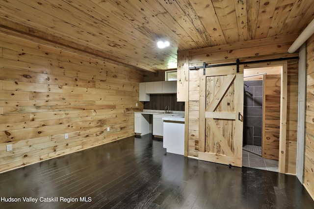 interior space featuring a barn door, dark hardwood / wood-style floors, white cabinetry, and wood walls