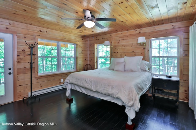 bedroom with wood walls, dark wood-type flooring, ceiling fan, access to exterior, and baseboard heating