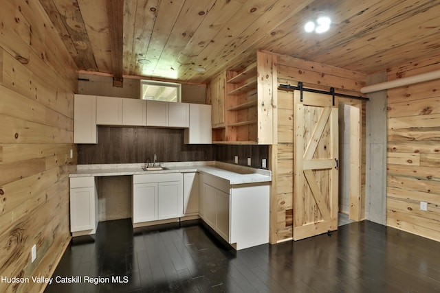 kitchen with white cabinetry, wooden ceiling, a barn door, dark hardwood / wood-style floors, and wood walls