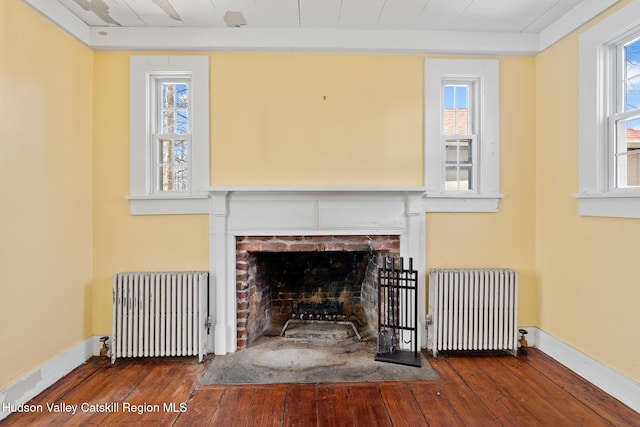 unfurnished living room featuring radiator, a brick fireplace, and plenty of natural light
