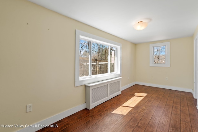 empty room featuring radiator heating unit, hardwood / wood-style flooring, and baseboards