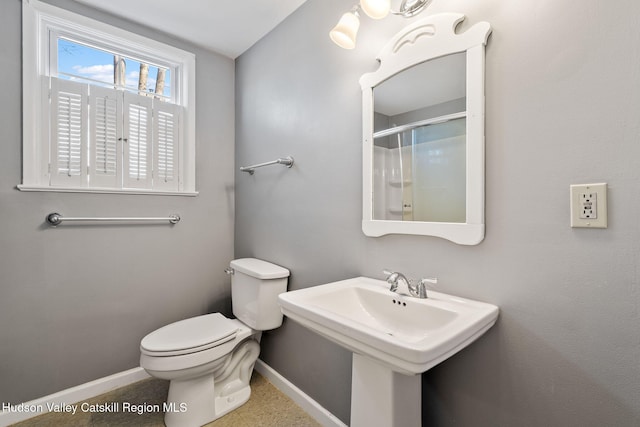 bathroom with toilet, a sink, baseboards, and a shower with door