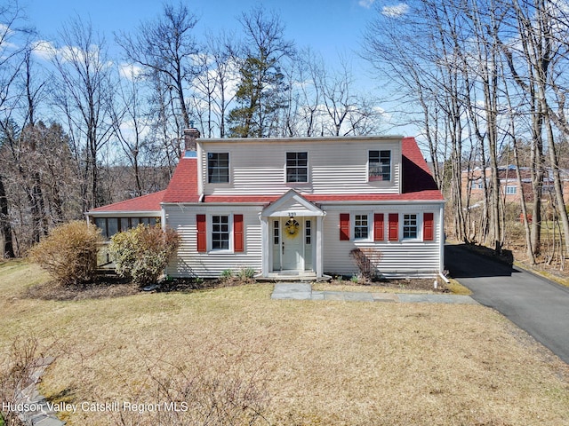 view of front facade featuring a shingled roof, a chimney, driveway, and a front lawn