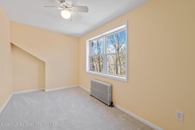 carpeted spare room featuring radiator, baseboards, and a ceiling fan