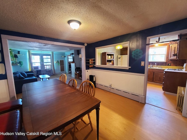 dining room with a baseboard heating unit, light wood finished floors, a textured ceiling, wainscoting, and plenty of natural light