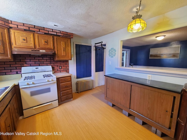 kitchen featuring a textured ceiling, radiator, white gas stove, brown cabinetry, and under cabinet range hood