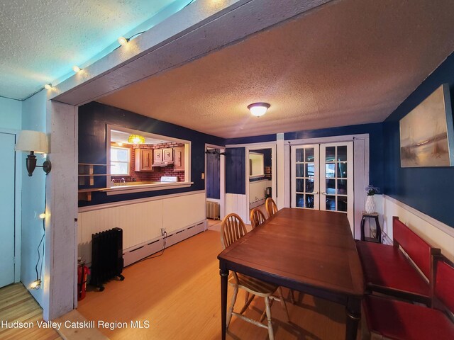 dining room with wood finished floors, french doors, a baseboard heating unit, wainscoting, and a textured ceiling