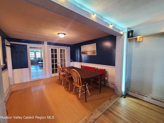 dining area featuring wainscoting, wood finished floors, french doors, and a textured ceiling