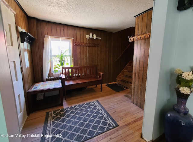 mudroom with light wood finished floors, wood walls, and a textured ceiling