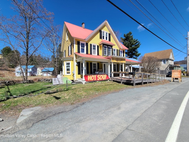 victorian home with a gambrel roof, a chimney, a front lawn, a porch, and metal roof