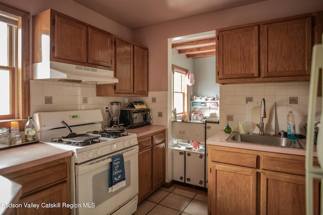 kitchen with sink, light tile patterned flooring, gas range gas stove, beam ceiling, and decorative backsplash