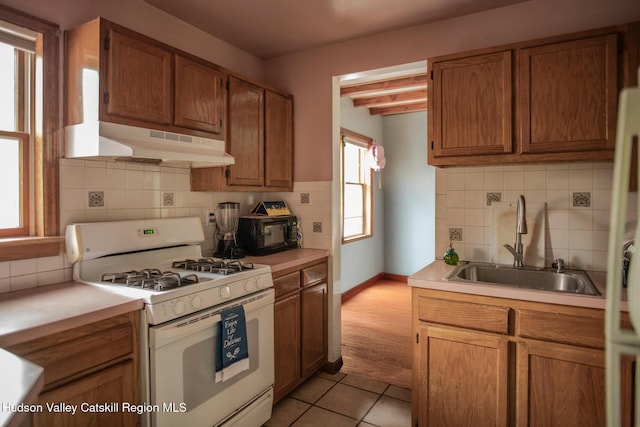 kitchen featuring sink, light tile patterned flooring, beamed ceiling, white gas range, and decorative backsplash