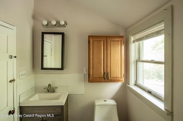 bathroom with toilet, vaulted ceiling, tile walls, and vanity