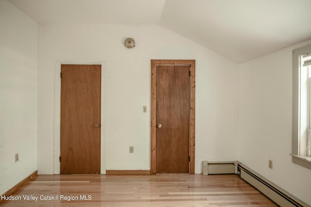 empty room with light hardwood / wood-style flooring, a baseboard heating unit, and lofted ceiling