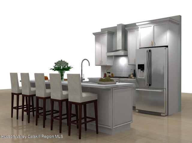 kitchen with gray cabinets, stainless steel fridge with ice dispenser, a center island with sink, and wall chimney range hood