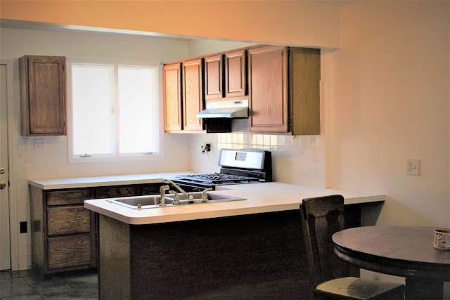 kitchen with kitchen peninsula, decorative backsplash, gas range, sink, and dark tile patterned flooring