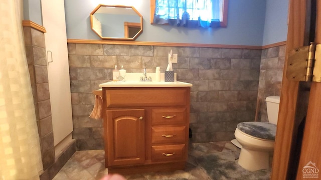 bathroom with toilet, tile walls, a wainscoted wall, and vanity