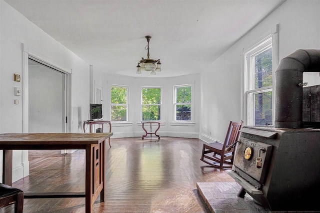 sitting room featuring dark wood-type flooring, a wood stove, a healthy amount of sunlight, and a notable chandelier