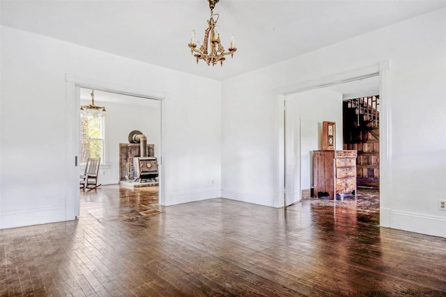 unfurnished room featuring wood-type flooring, a wood stove, and a chandelier