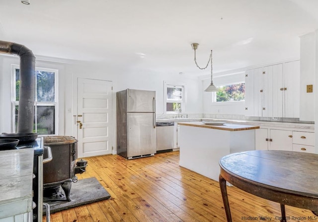 kitchen with light wood-type flooring, stainless steel appliances, decorative light fixtures, white cabinets, and a wood stove