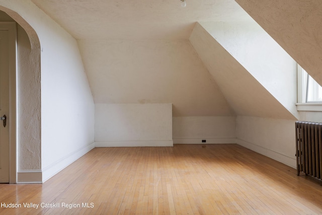 additional living space with light wood-type flooring, radiator, and vaulted ceiling