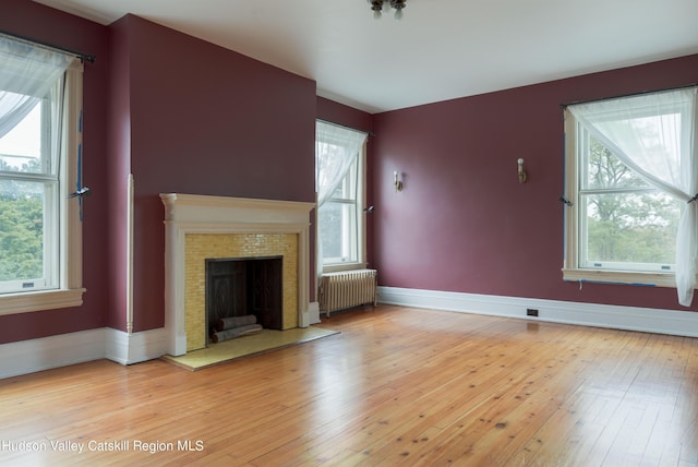 unfurnished living room featuring a fireplace, radiator heating unit, and light hardwood / wood-style floors