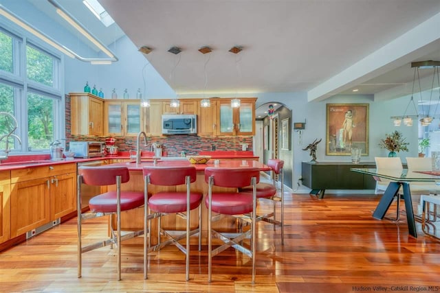kitchen with light wood-type flooring, a sink, stainless steel microwave, and backsplash