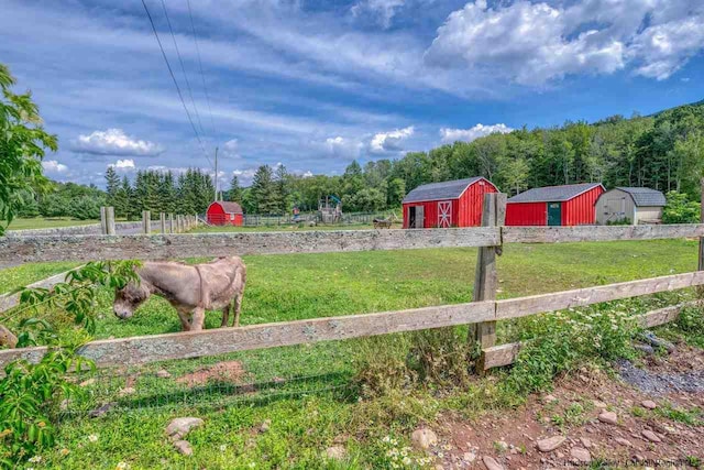 view of yard featuring a storage shed, a wooded view, fence, and an outbuilding
