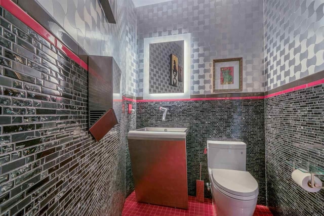 half bathroom with tile patterned flooring, vanity, toilet, tile walls, and a wainscoted wall