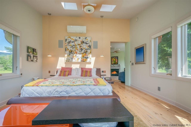 bedroom featuring an AC wall unit, a skylight, multiple windows, and light wood-style floors