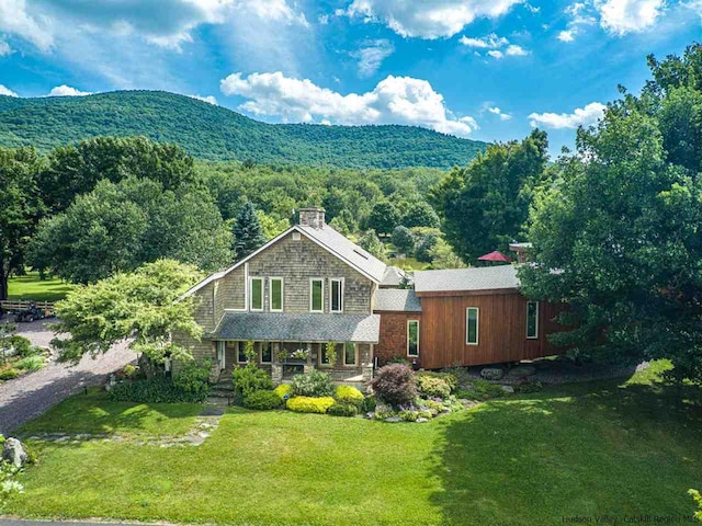 view of front of house with a view of trees, a mountain view, a front yard, and a chimney