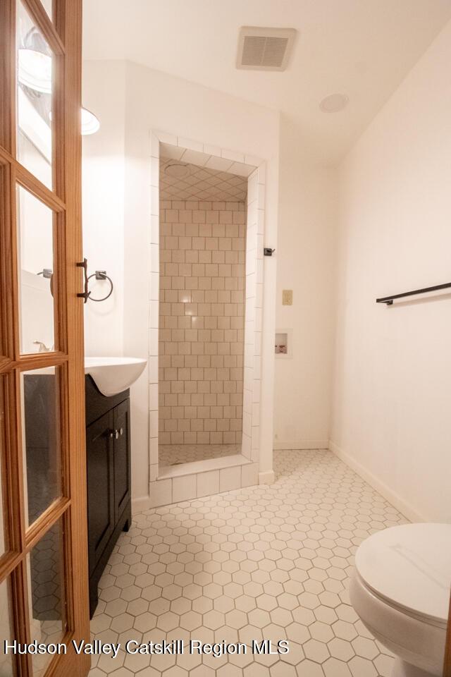 bathroom featuring tile patterned flooring, vanity, toilet, and tiled shower