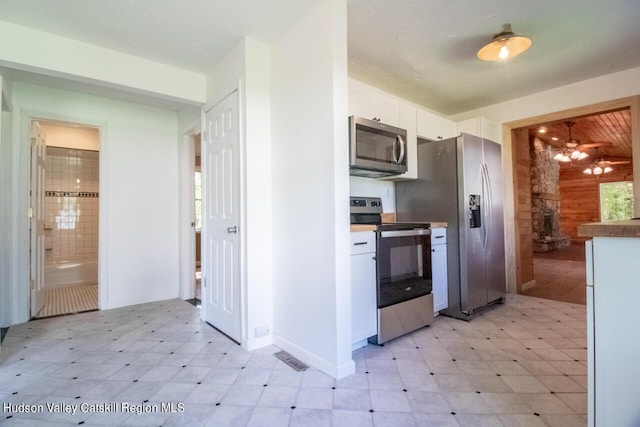 kitchen featuring ceiling fan, white cabinets, stainless steel appliances, and wood walls