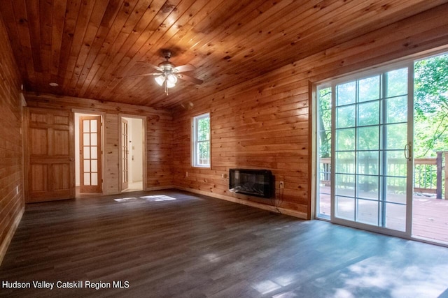 unfurnished living room featuring wooden walls, ceiling fan, a large fireplace, dark hardwood / wood-style flooring, and wood ceiling