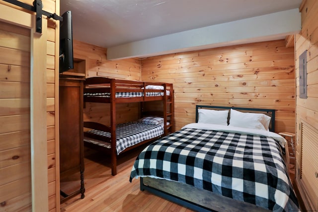 bedroom featuring light wood-style floors, wood walls, and a barn door