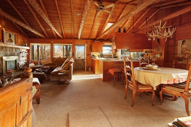 carpeted dining area featuring wooden walls, vaulted ceiling with beams, ceiling fan, a fireplace, and wood ceiling