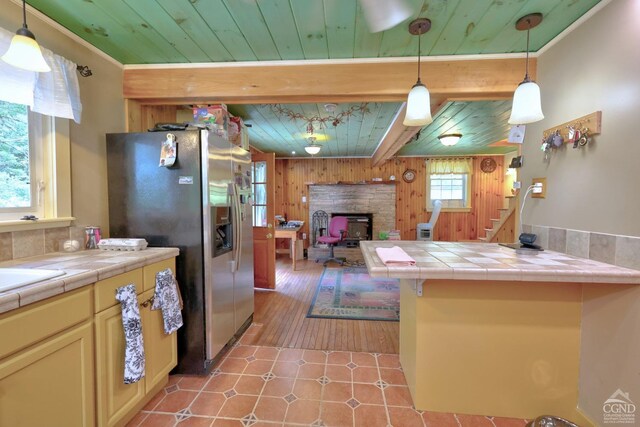 630 County Route 11, Ancram, NY 12502 - kitchen with stainless steel refrigerator with ice dispenser, tile counters, wood walls, a fireplace, and wooden ceiling