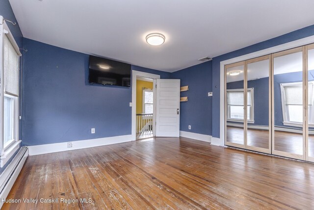 empty room featuring a baseboard radiator, wood-type flooring, baseboards, and visible vents