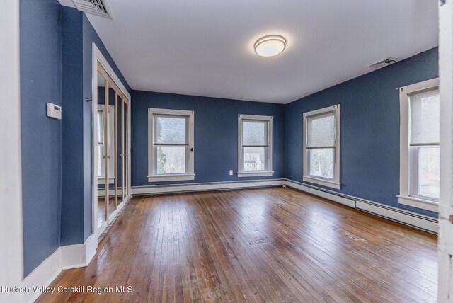 empty room with baseboards, baseboard heating, visible vents, and wood-type flooring