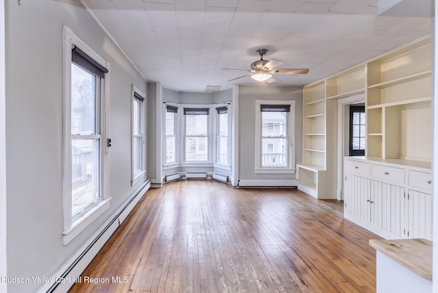 unfurnished living room with ceiling fan, a baseboard heating unit, hardwood / wood-style flooring, and built in shelves
