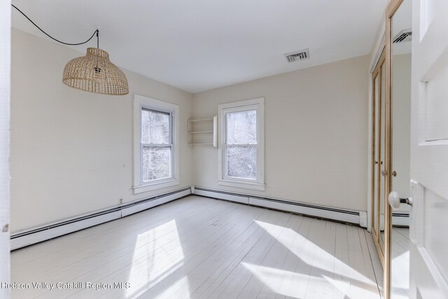 empty room with a baseboard radiator, visible vents, and wood finished floors