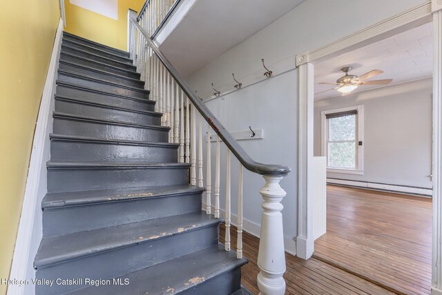 staircase featuring baseboards, ceiling fan, wood finished floors, and baseboard heating