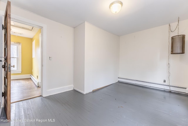 spare room with baseboards, a baseboard heating unit, and wood-type flooring