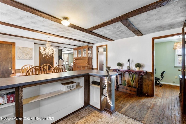 kitchen featuring beamed ceiling, an inviting chandelier, dark countertops, baseboards, and hardwood / wood-style flooring